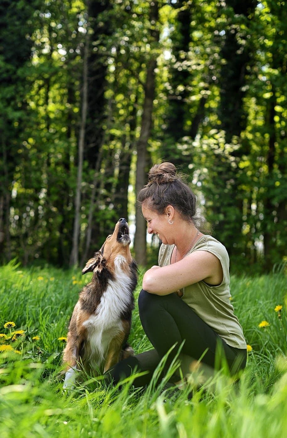 Marion und ihr Hund gemeinsam auf einer grünen Wiese am Waldrand